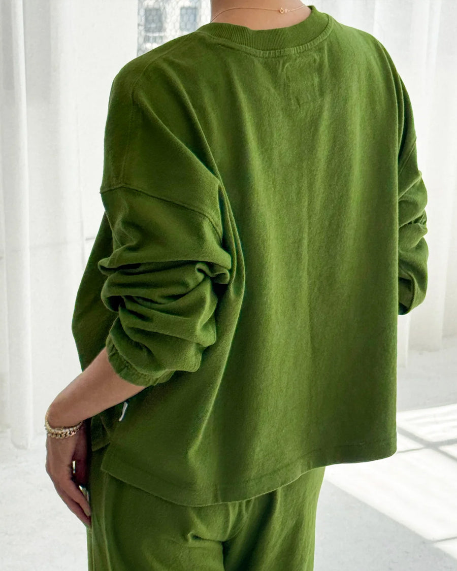 back view of model wearing avocado colored long sleeve tee with elastic wristbands