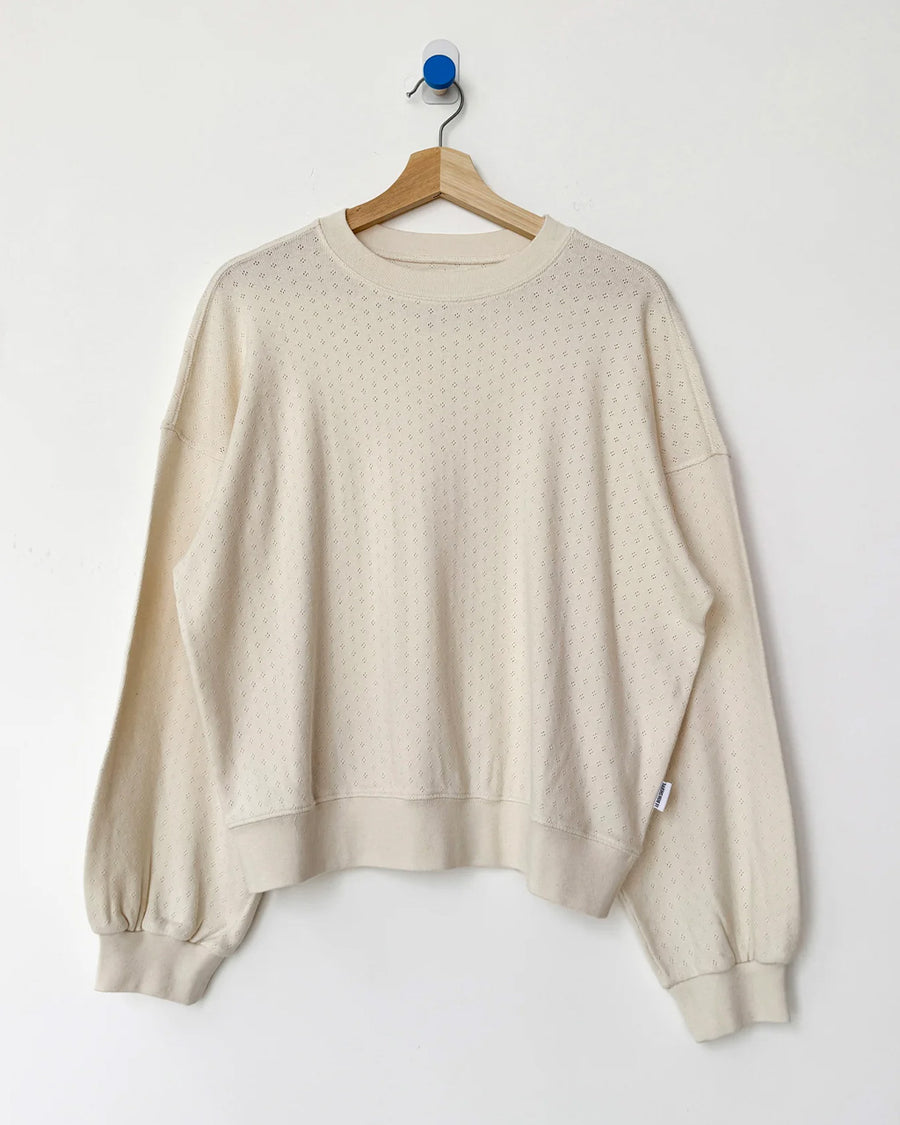 cream pointelle long sleeve sweatshirt with banded wrists and waist on a hanger