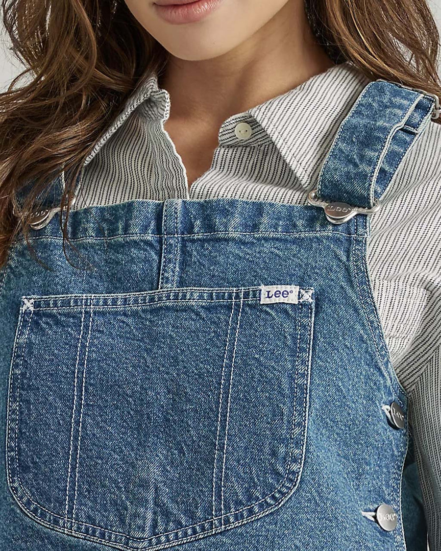 up close of model wearing denim overall bib top with adjustable straps, cropped length and front pocket