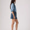 side view of model wearing medium blue mini denim skirt with pin tucked denim blouse