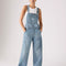 model wearing light denim relaxed fit overalls with front pockets