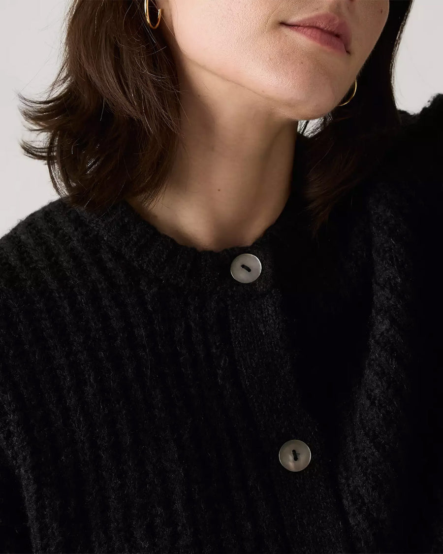 up close of model wearing black textured cardigan with shell buttons