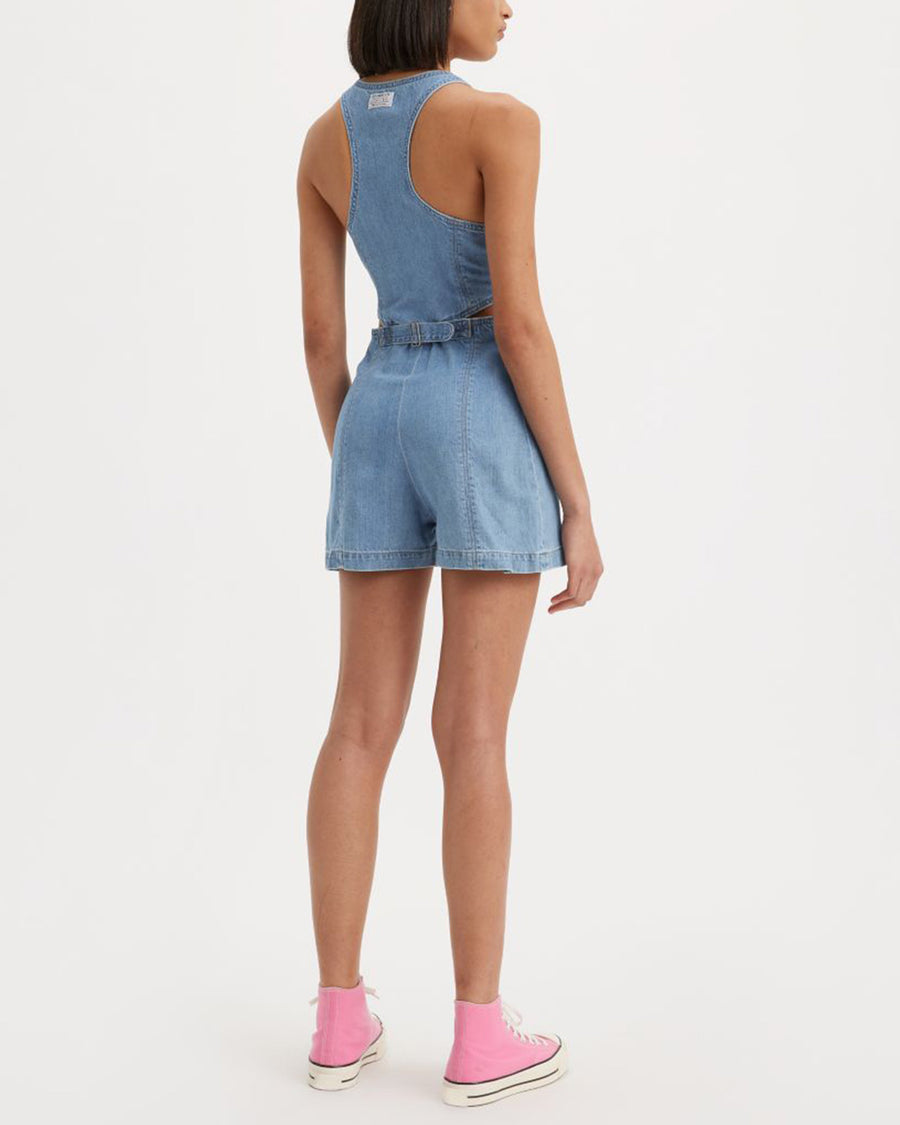 backview of model wearing light denim romper with zip front and cut out sides