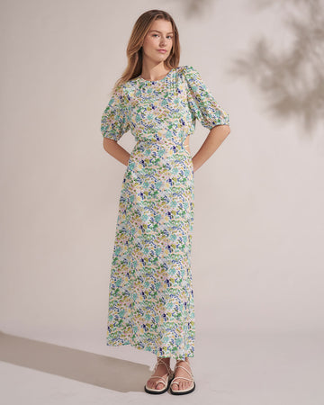 model wearing white maxi dress with slight puff sleeves, all over floral print and open tie back