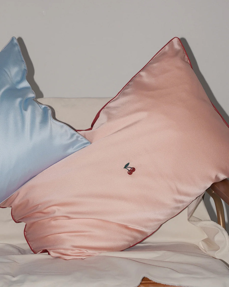 pink mulberry silk pillowcase with  embroidered cherries in the center on a bed