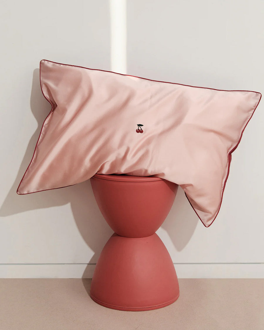 pink mulberry silk pillowcase with  embroidered cherries in the center on a table