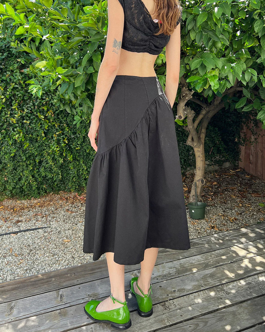 back view of model wearing black twill midi skirt with wavey hem detail