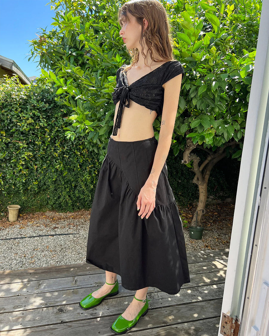 side view of model wearing black twill midi skirt with wavey hem detail