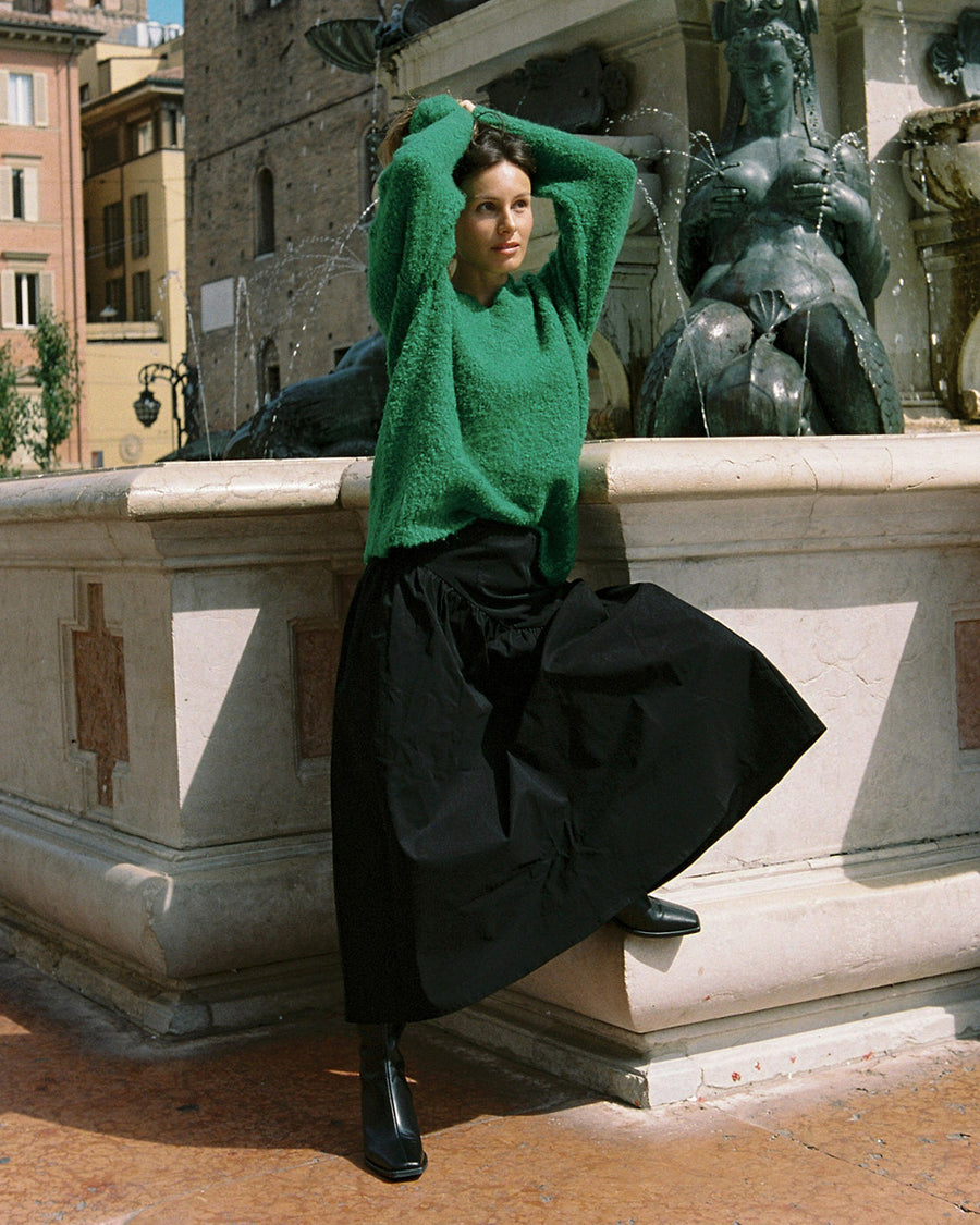 side view of model wearing green textured v-neck sweater and twill skirt