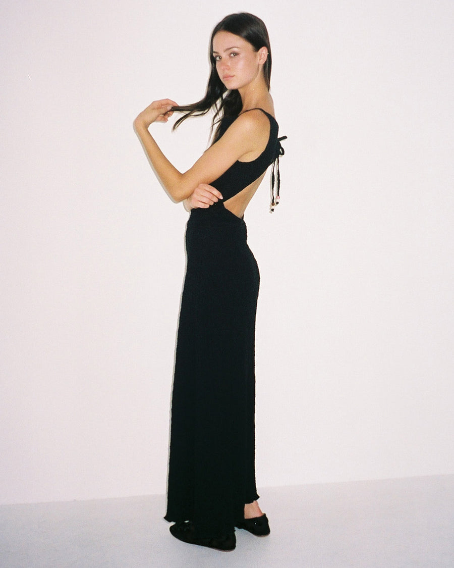 side view of model wearing black crinkle maxi dress with asymmetrical hem and open back