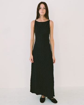 model wearing black crinkle maxi dress with asymmetrical hem and open back