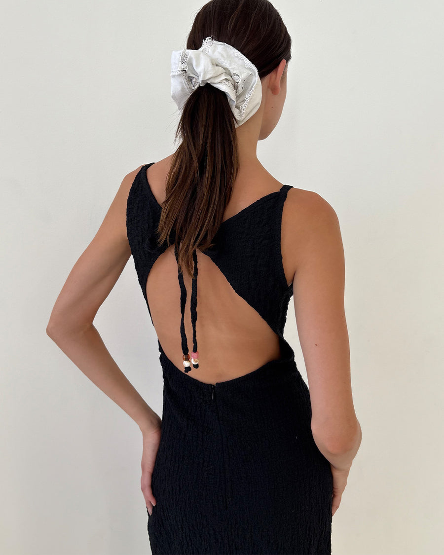 back view of model wearing black crinkle maxi dress with asymmetrical hem and open back