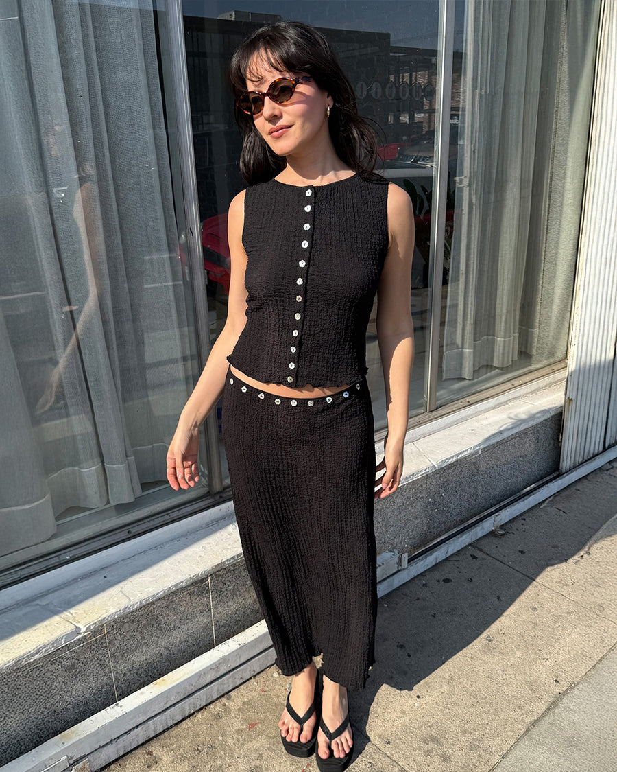 model wearing black crinkle midi skirt with shaped shell buttons on the top and matching tank