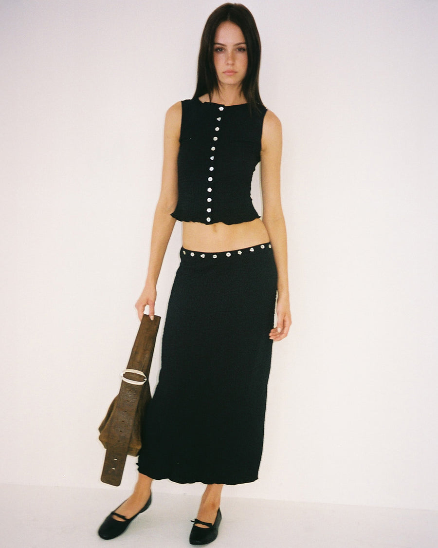model wearing black crinkle midi skirt with shaped shell buttons on the top and matching tank