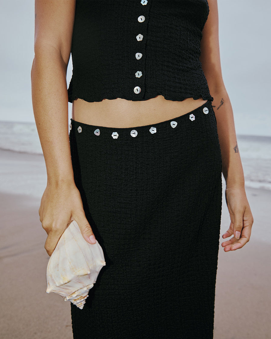 up close of model wearing black crinkle midi skirt with shaped shell buttons on the top and matching tank
