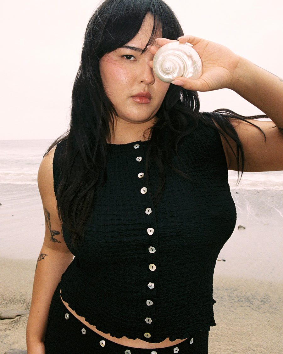 model wearing cropped black crinkle button front tank with various shaped shell buttons