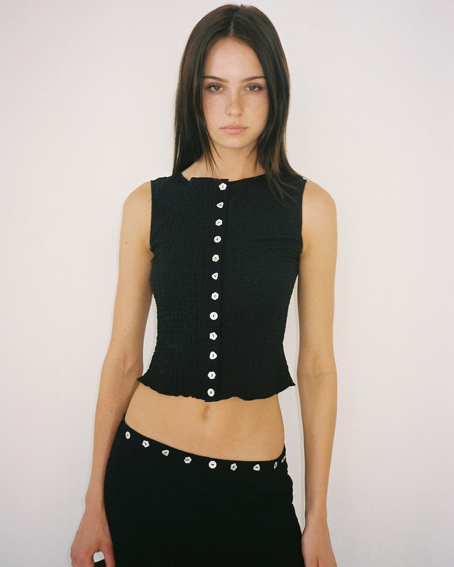 model wearing cropped black crinkle button front tank with various shaped shell buttons