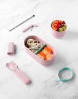 circular pink bamboo snack box with mint elastic closure on table with other styles