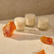 The Le Long Fond candle by Maison Louis Marie is white and comes in a clear glass tumbler. surrounded by pieces of amber