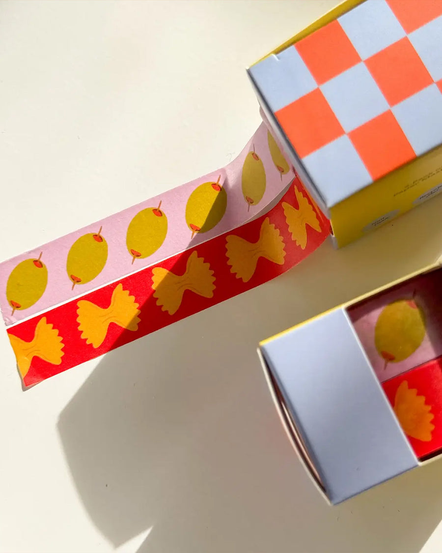 set of two rolls of washi tape: pink tape with olives, and red with bowtie pasta on the table