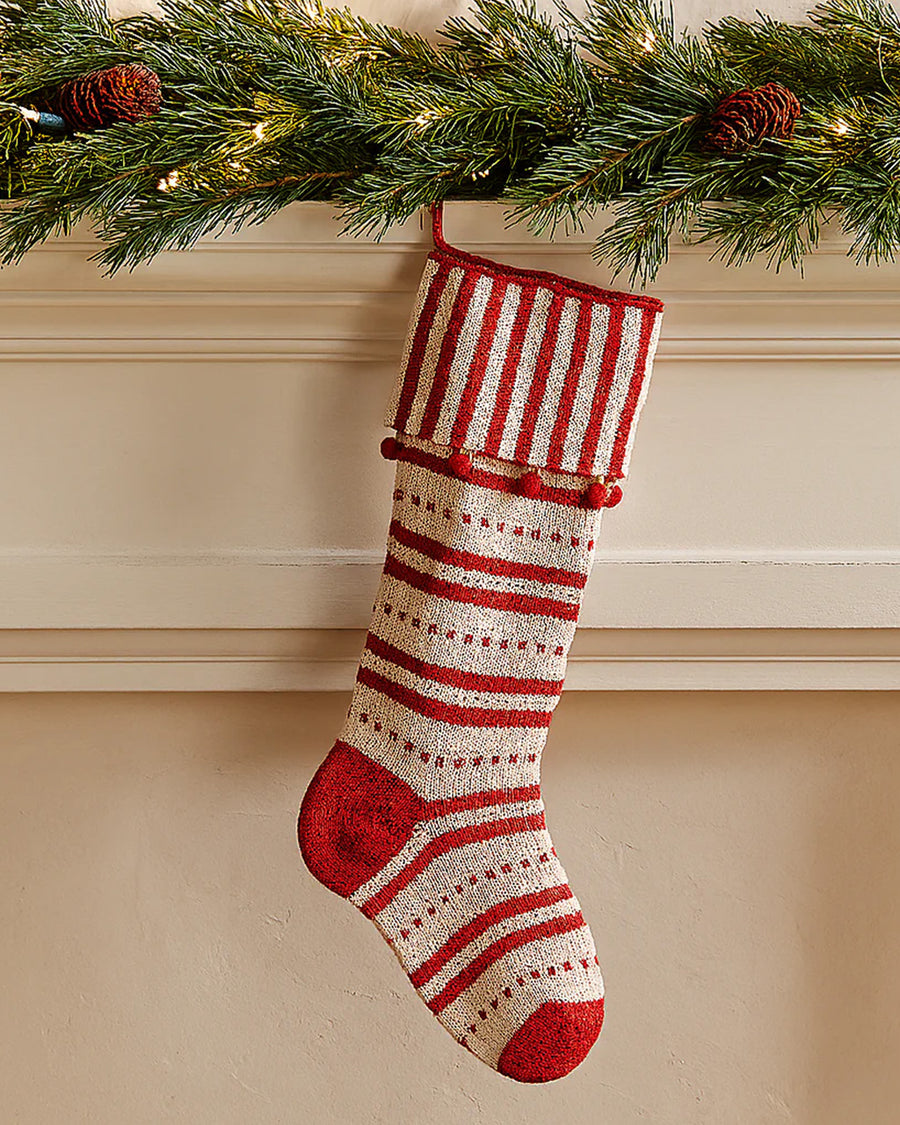 cream and red striped stocking with striped cuff and red pom detail hanging from a mantle
