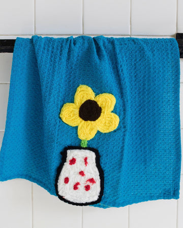 blue towel with yarn flower and flower vase graphic near the bottom