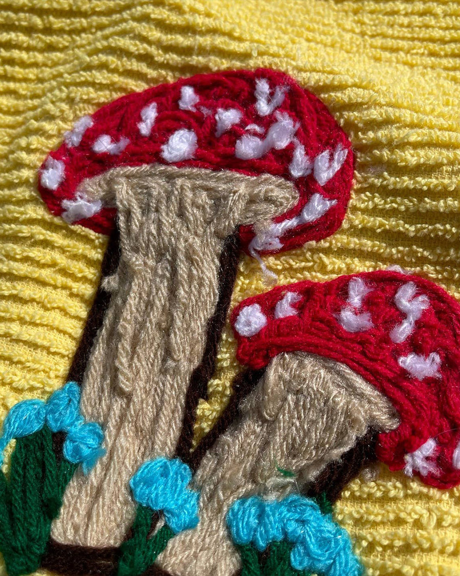 up close of yellow towel with yarn red mushroom design near the bottom