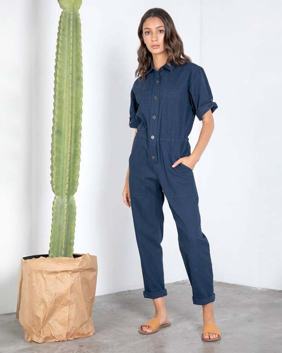 model wearing dark blue short sleeve jumpsuit with cinched waist and button front