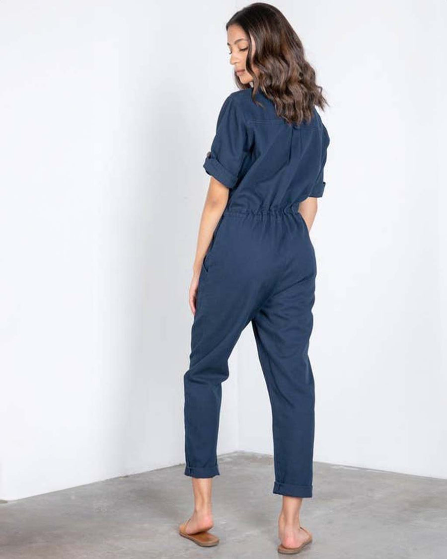 back view of model wearing dark blue short sleeve jumpsuit with cinched waist and button front