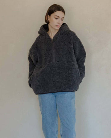 model wearing charcoal sherpa sweater with quarter zip, hood, and elbow patches