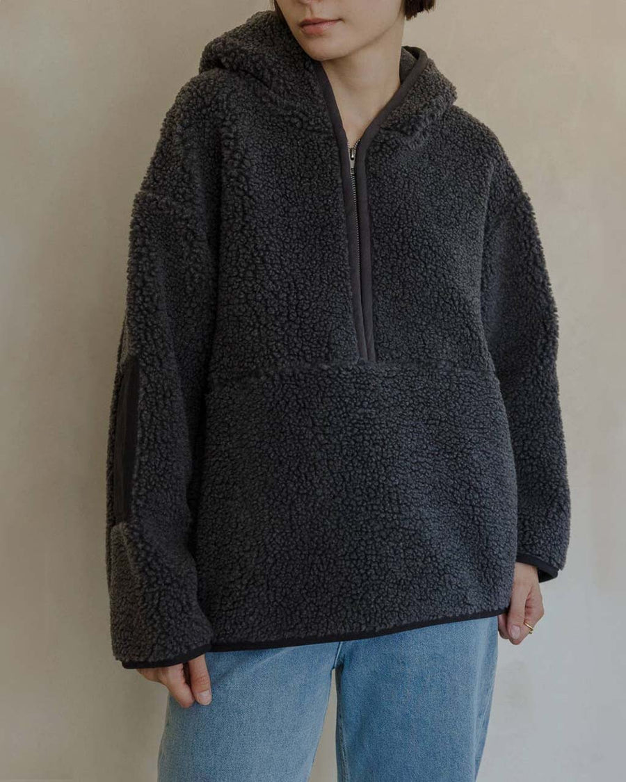 up close of model wearing charcoal sherpa sweater with quarter zip, hood, and elbow patches
