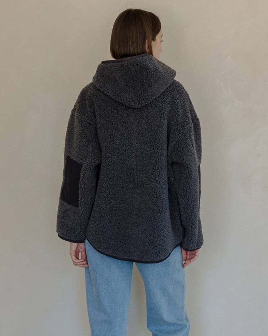 back view of model wearing charcoal sherpa sweater with quarter zip, hood, and elbow patches