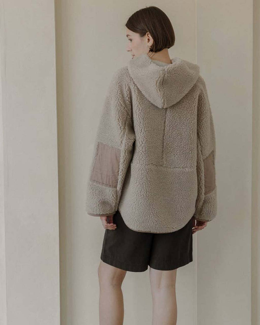 back view of model wearing taupe sherpa sweater with quarter zip, hood, and elbow patches
