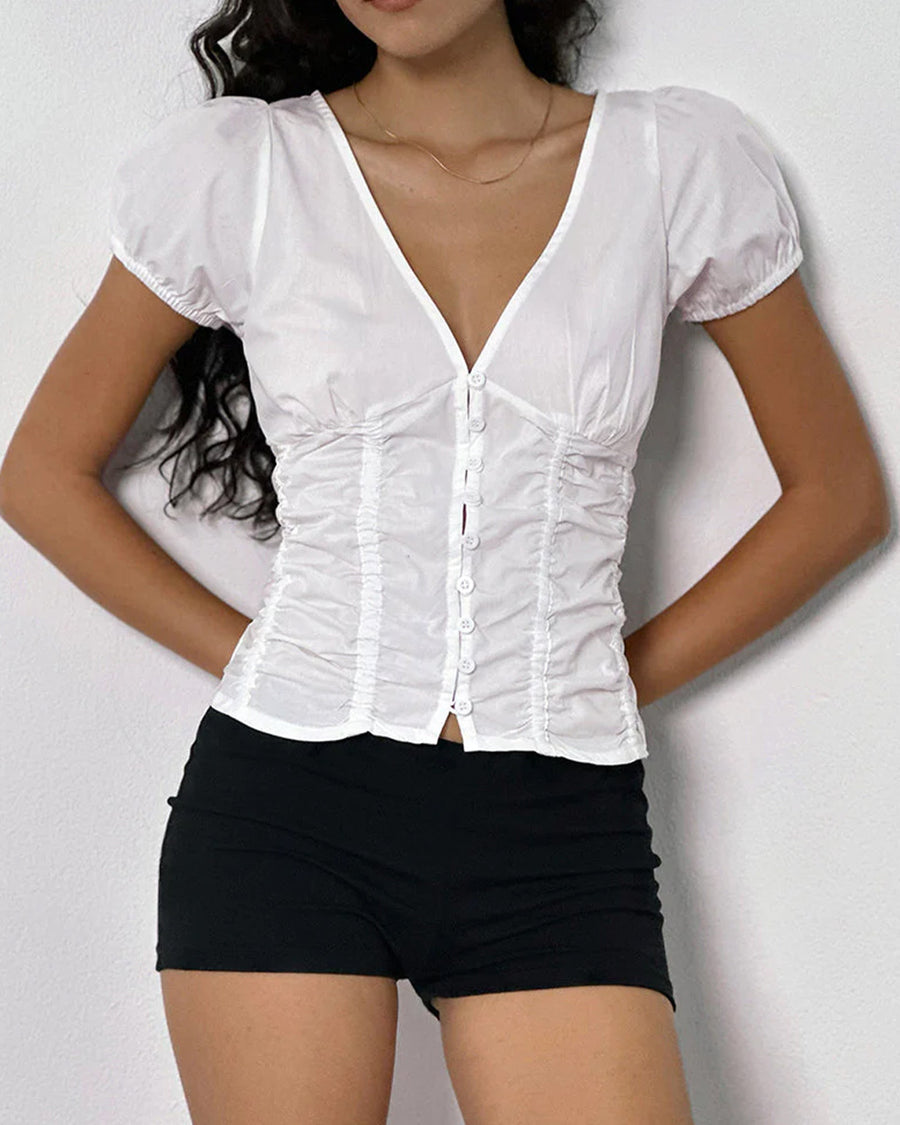 up close of model wearing white cotton short sleeve blouse with deep v-neck, button front and corset waist and black shorts