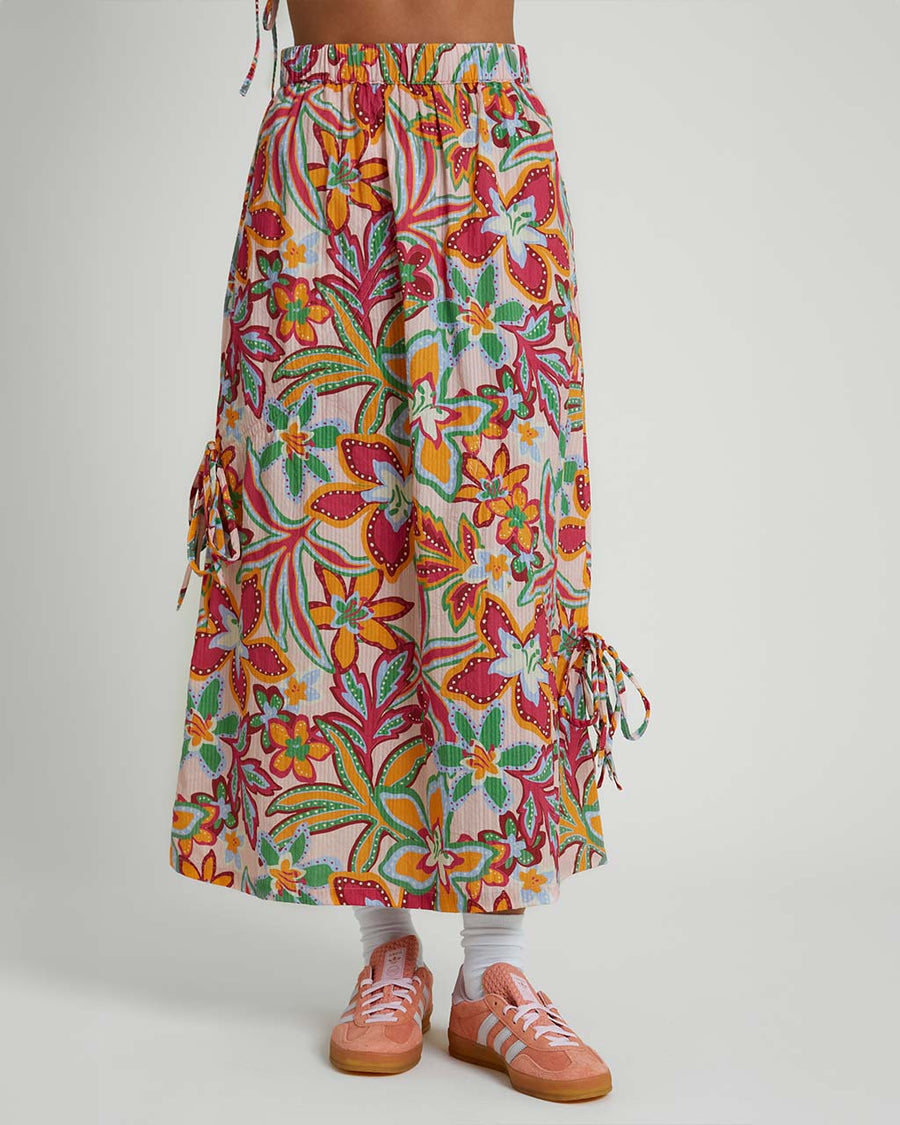 model wearing light pink midiaxi skirt with elastic waist, side ties and colorful abstract floral print