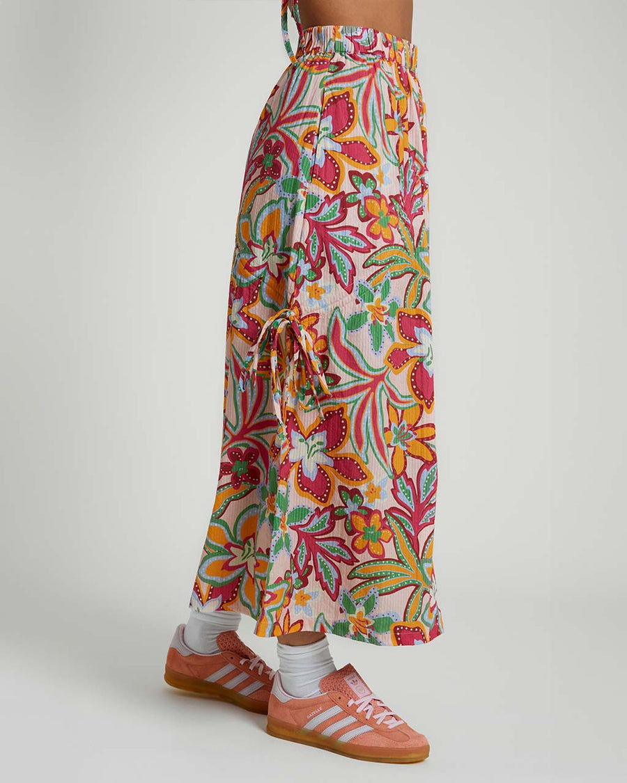 side view of model wearing light pink midiaxi skirt with elastic waist, side ties and colorful abstract floral print