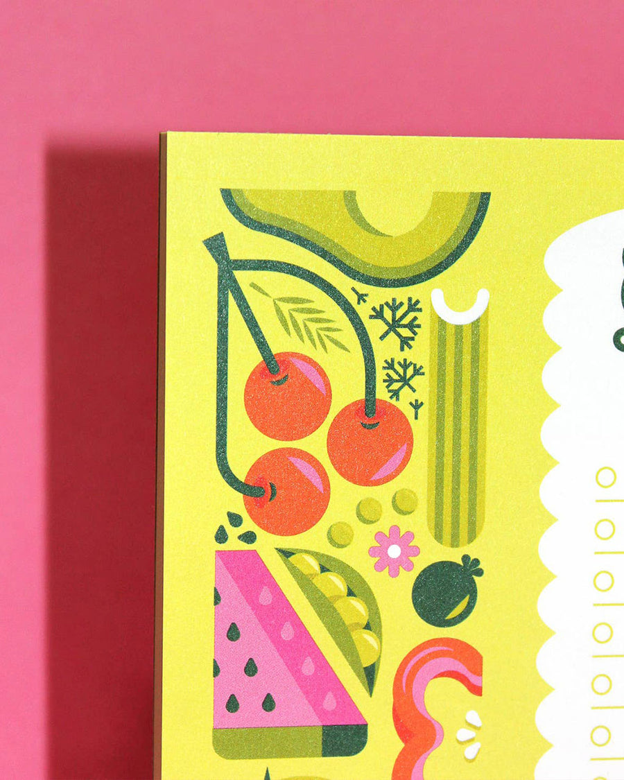 up close of lined grocery list notepad with slightly glittery fruits and veggies on the side