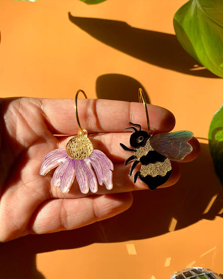 model holding mix-match earrings: one pink flower dangle, and the other bee dangle