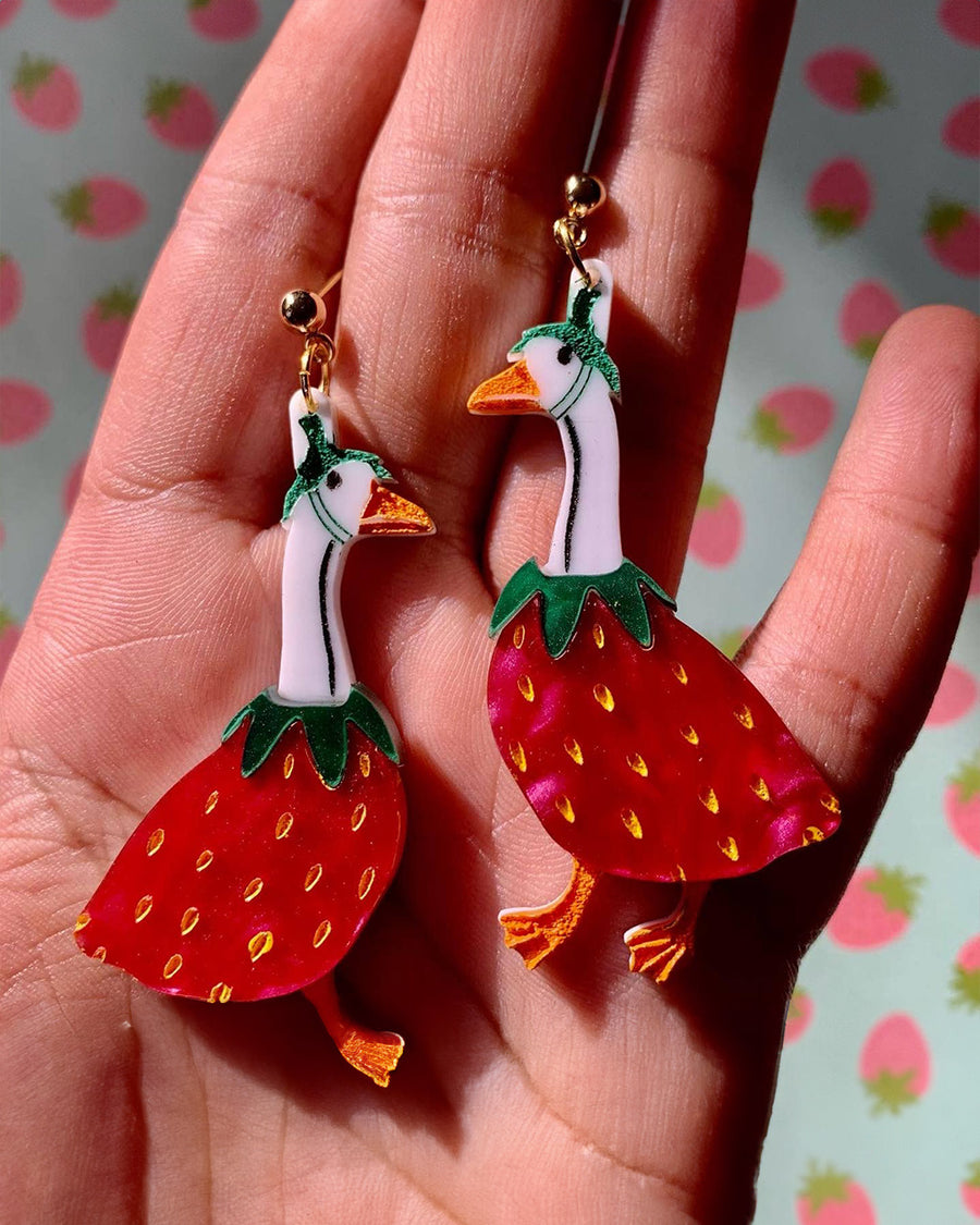 model holding large dangle earrings with geese dressed as a strawberry