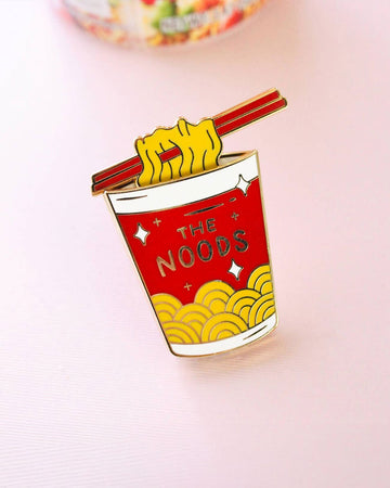 interactive enamel pin with red 'the noods' container and moveable noodle piece