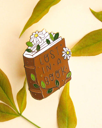 book shaped pin with daisies popping out and says 'lost in a book' across the front