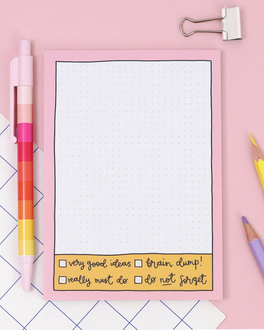 grid notepad with pink border and bottom checklist next to desk items