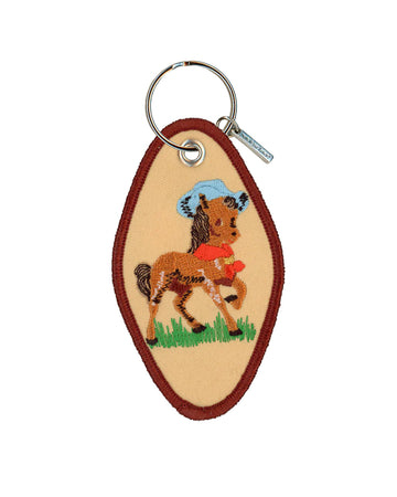 tan hotel keychain with brown trim and pony with a blue cowboy hat on