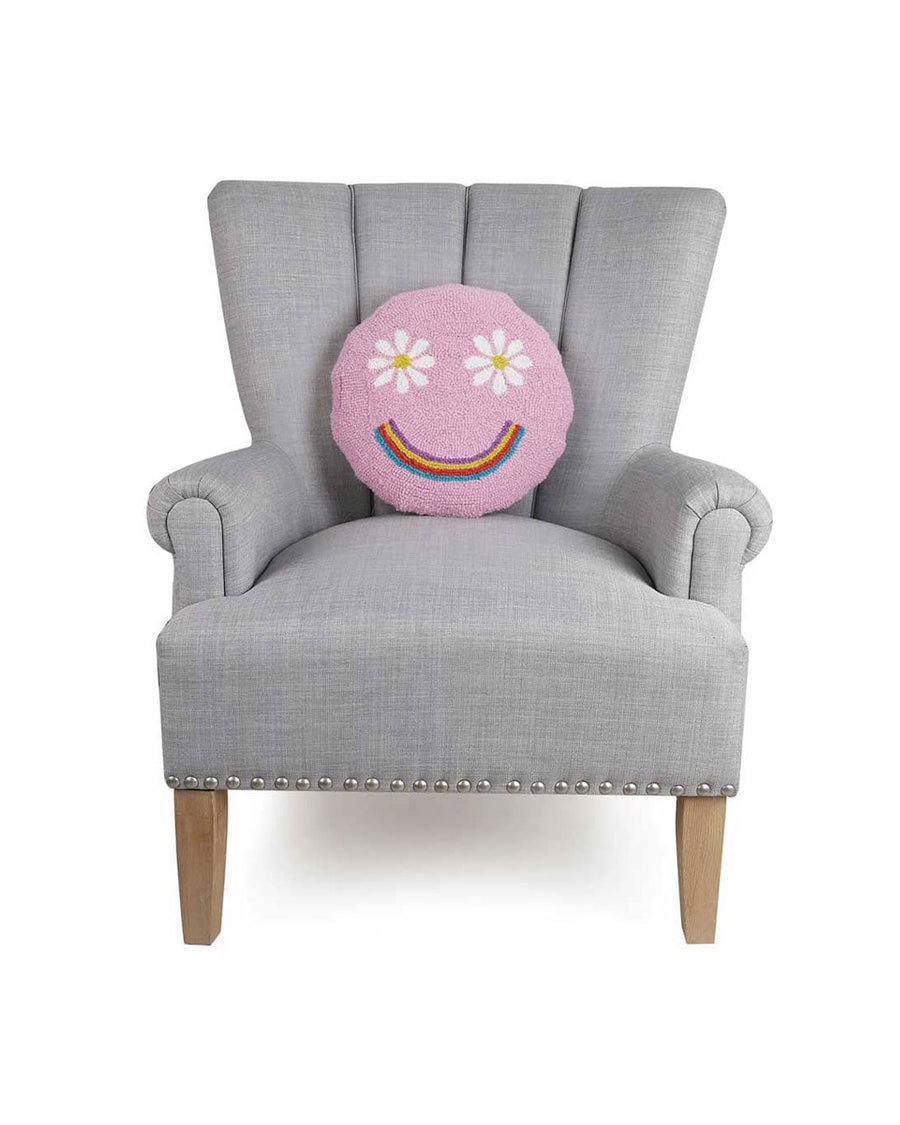 pink round smiley face pillow with flower eyes and rainbow smile on chair