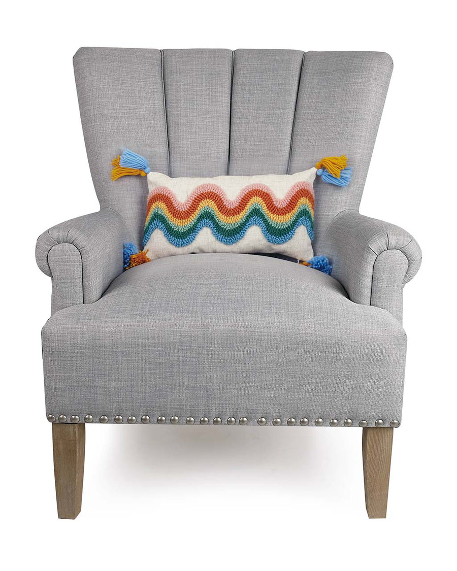 white throw pillow with wavy rainbow print and blue and yellow tassels on a grey chair