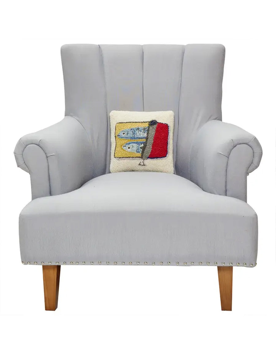 cream square throw pillow with two sardines in a red tin on a chair
