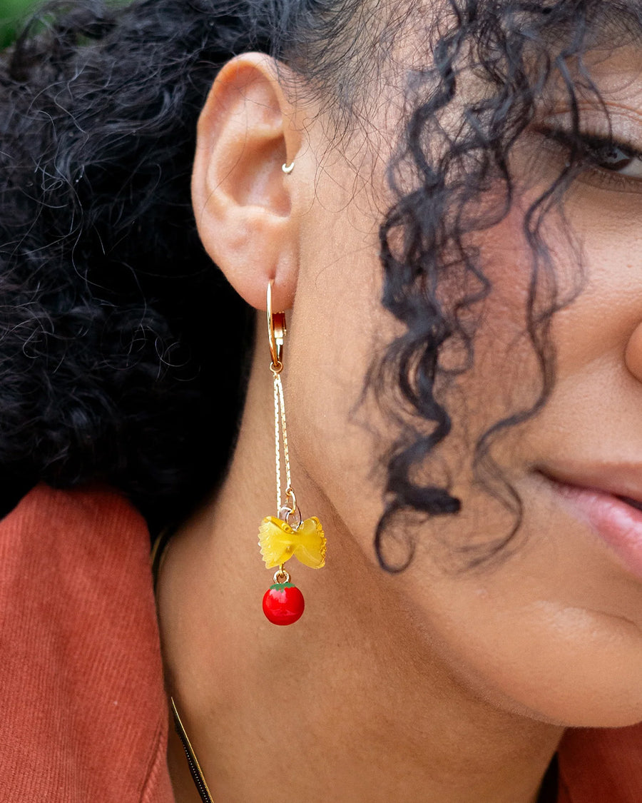 up close of model wearing dangle earrings with bow-tie pasta and tomato charms