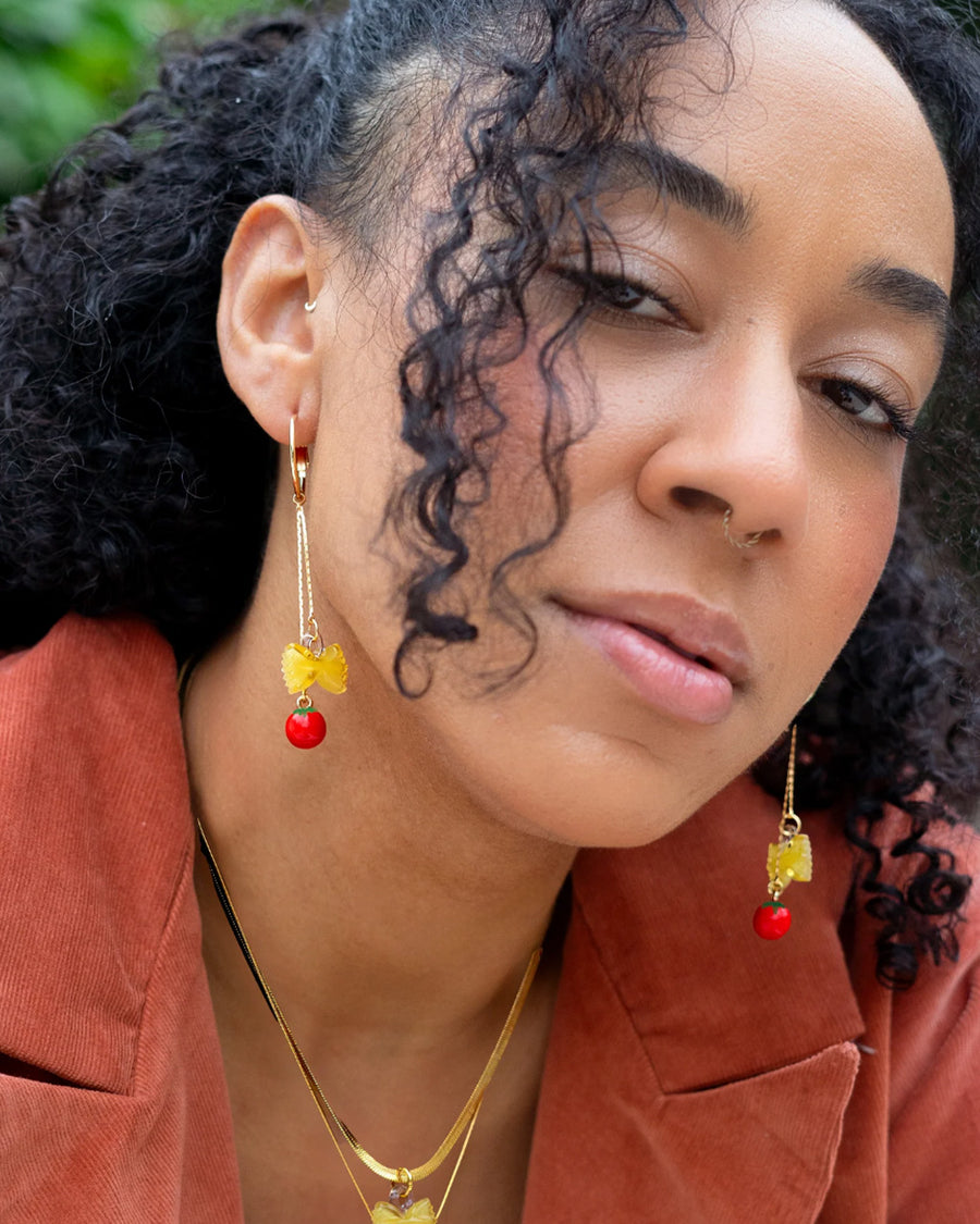 model wearing dangle earrings with bow-tie pasta and tomato charms