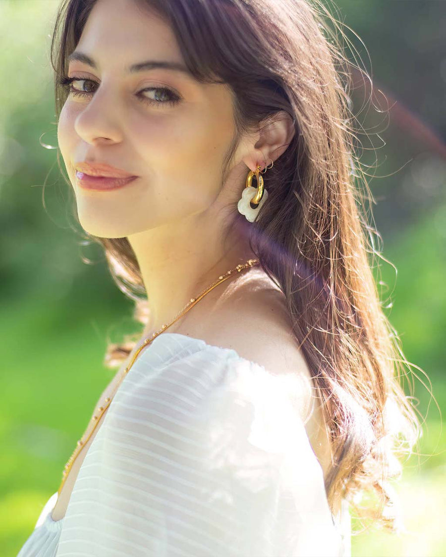 model wearing thick gold hoop earrings with acrylic white flower charm