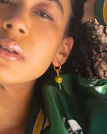 model wearing green olive hoop dangle earrings with a gold 'toothpick' through it
